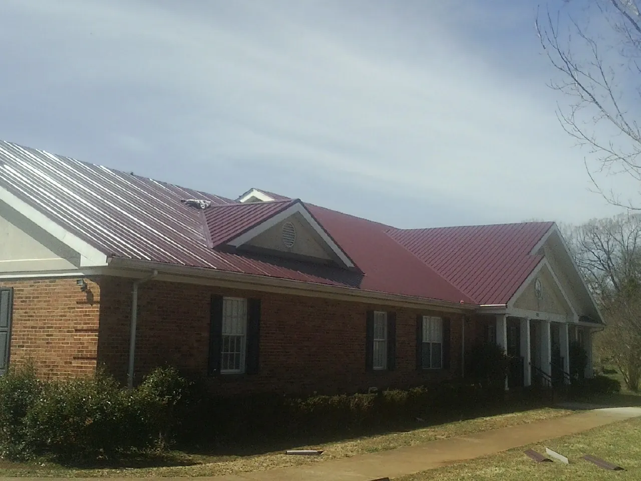 Red metal roof with gabled entries on a long brick building, from a Hail Damage Roof Repair job in Elma