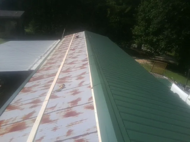 Old rusted panels beside newly installed green metal roofing — Wind Damage Roof Repair by Roofing Brothers in Elma