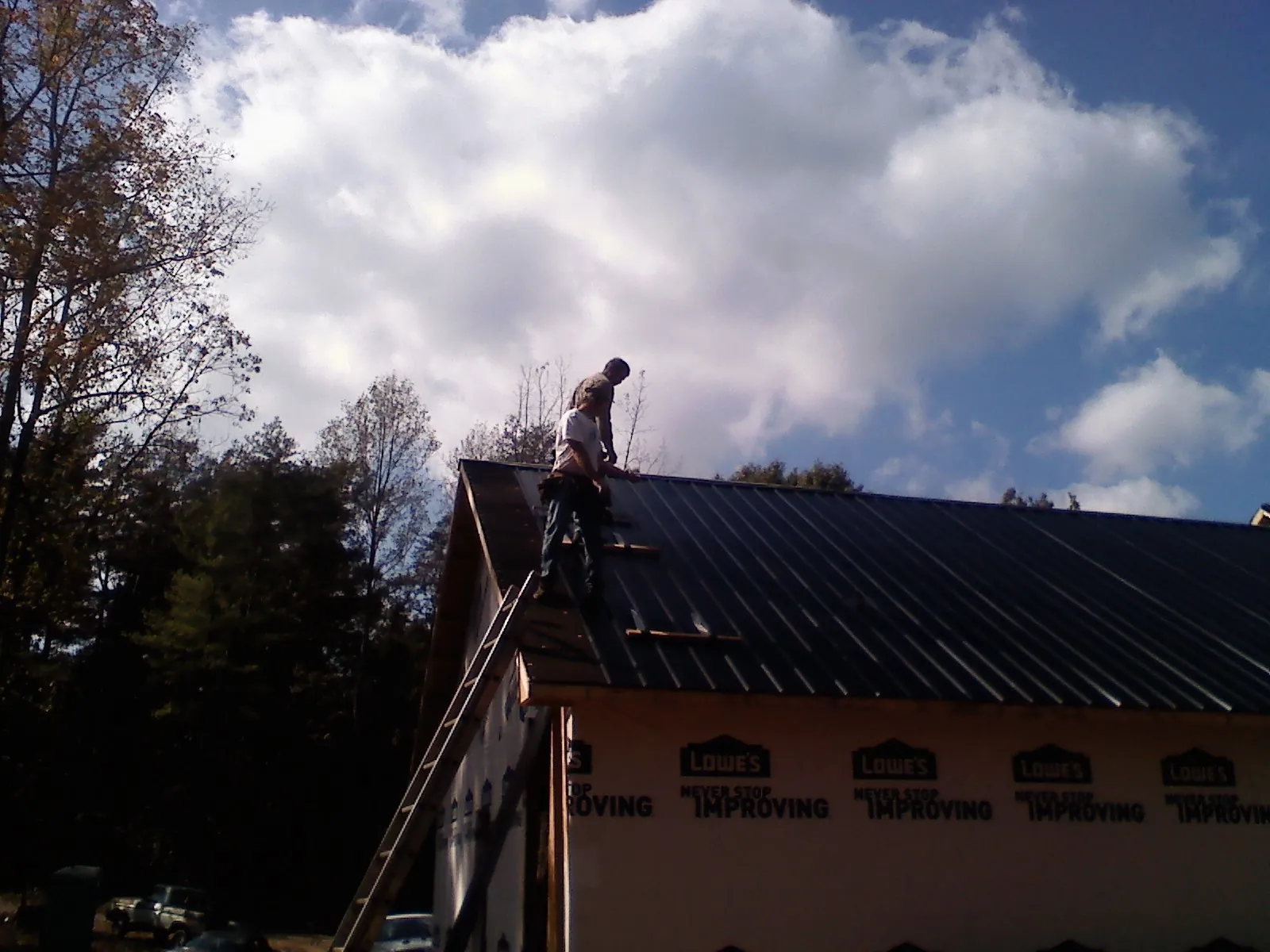 Roofer fastening dark metal panels high against a cloudy sky, from a Roof Inspection job in Elma