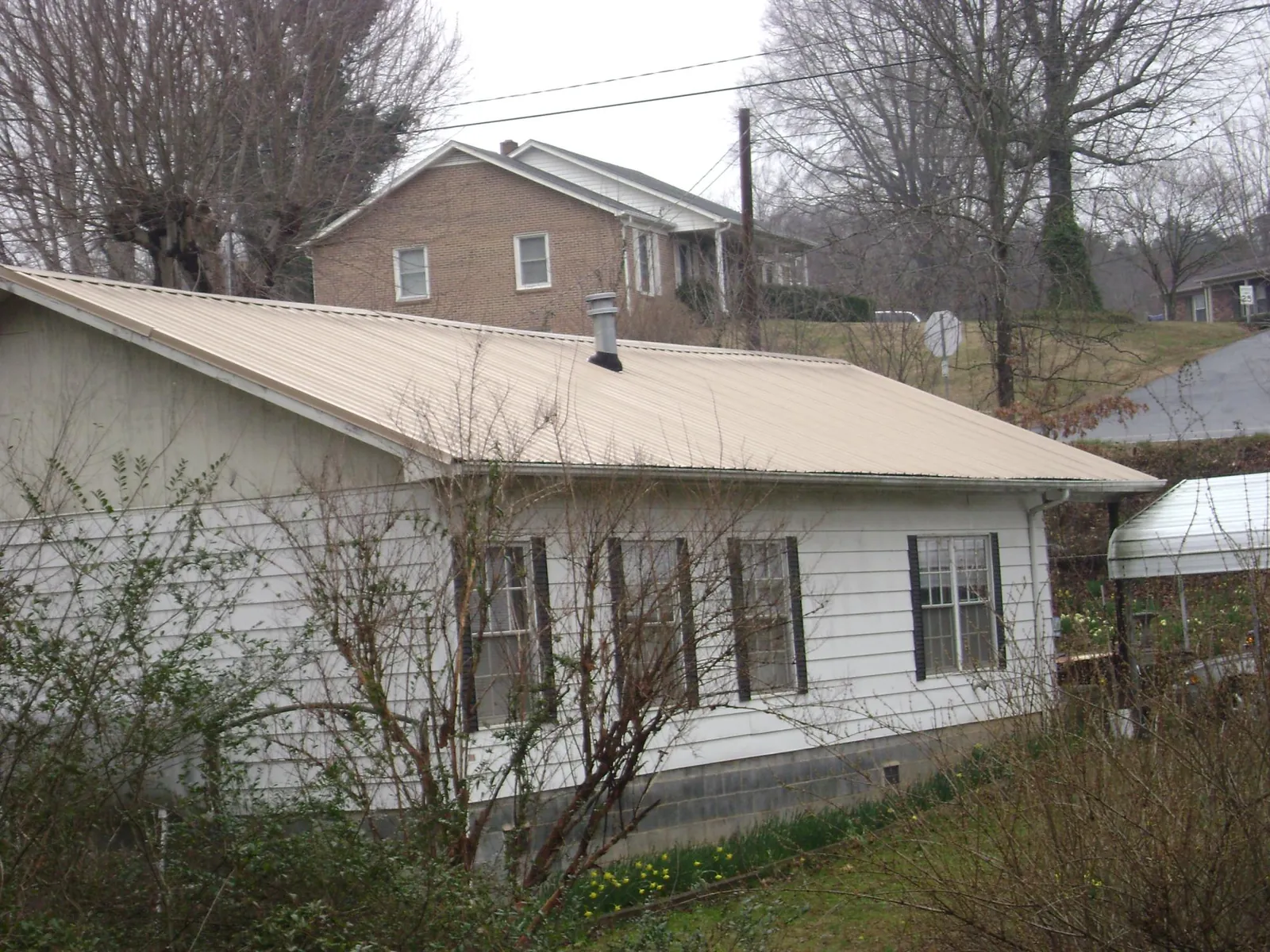 Tan metal roof on a white sided house set into a hillside — Commercial Roofing by Roofing Brothers in Elma